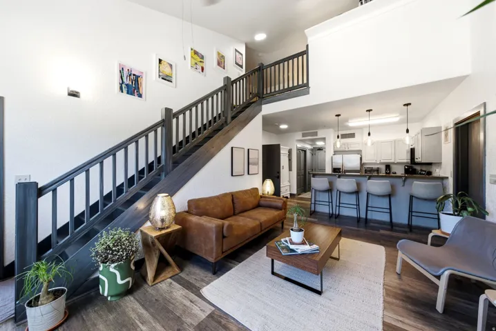 Open-concept living space featuring wood-finish flooring, a contemporary staircase with dark wood railing, and a kitchen island with built-in seating