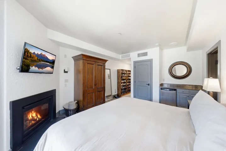 Bedroom featuring a built-in fireplace, wall-mounted television, and a custom built-in bar area with a compact refrigerator