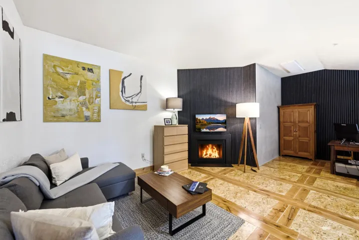 Living area featuring a floor-mounted fireplace, dark fluted accent walls, light wood-finish flooring, white walls, and a recessed ceiling light