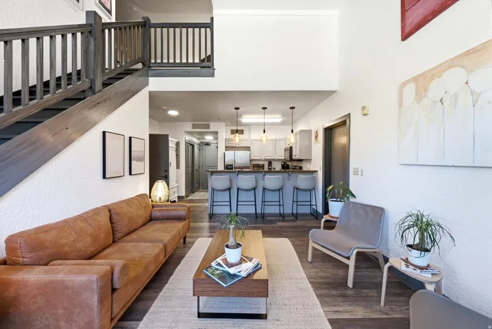 Open-concept living space featuring wood-finish flooring, a contemporary staircase with dark wood balusters, and high ceilings