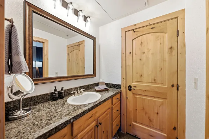 Bathroom featuring a natural wood vanity with an integrated sink, a granite-finish countertop, and a large framed mirror