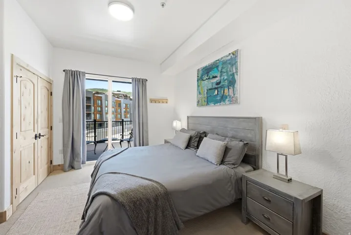 Bedroom featuring light-colored wood panel doors with black hardware, a balcony with black wrought iron railing, and carpeting