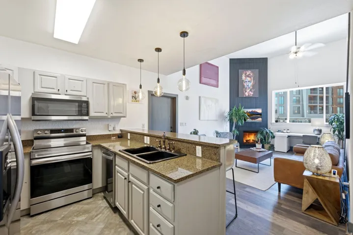 Open-concept kitchen featuring granite countertops, stainless steel appliances, a double basin sink, and pendant lighting