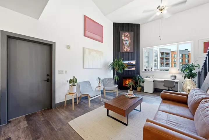 Living area featuring a vaulted ceiling with a ceiling fan, wood-finish flooring, a built-in fireplace, a built-in desk, and a large window