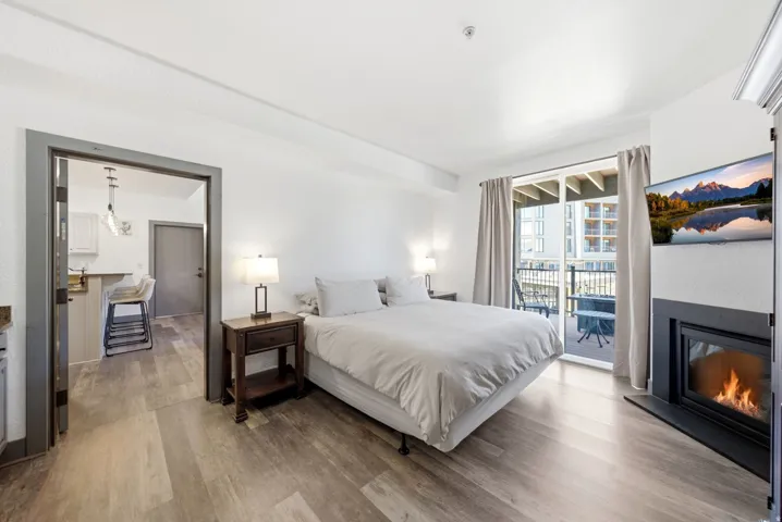 Open-concept living area featuring wood-finish flooring, a built-in fireplace with a black hearth, and a glass-paneled door opening to an exterior balcony