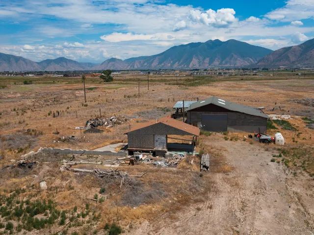 Expansive undeveloped land featuring multiple existing structures, including a barn with a metal roof and a partially constructed building with a shingled roof