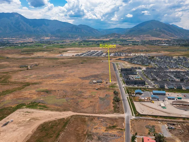 Expansive land parcel featuring undeveloped terrain with street frontage, surrounded by established residential developments and distant mountainous topography