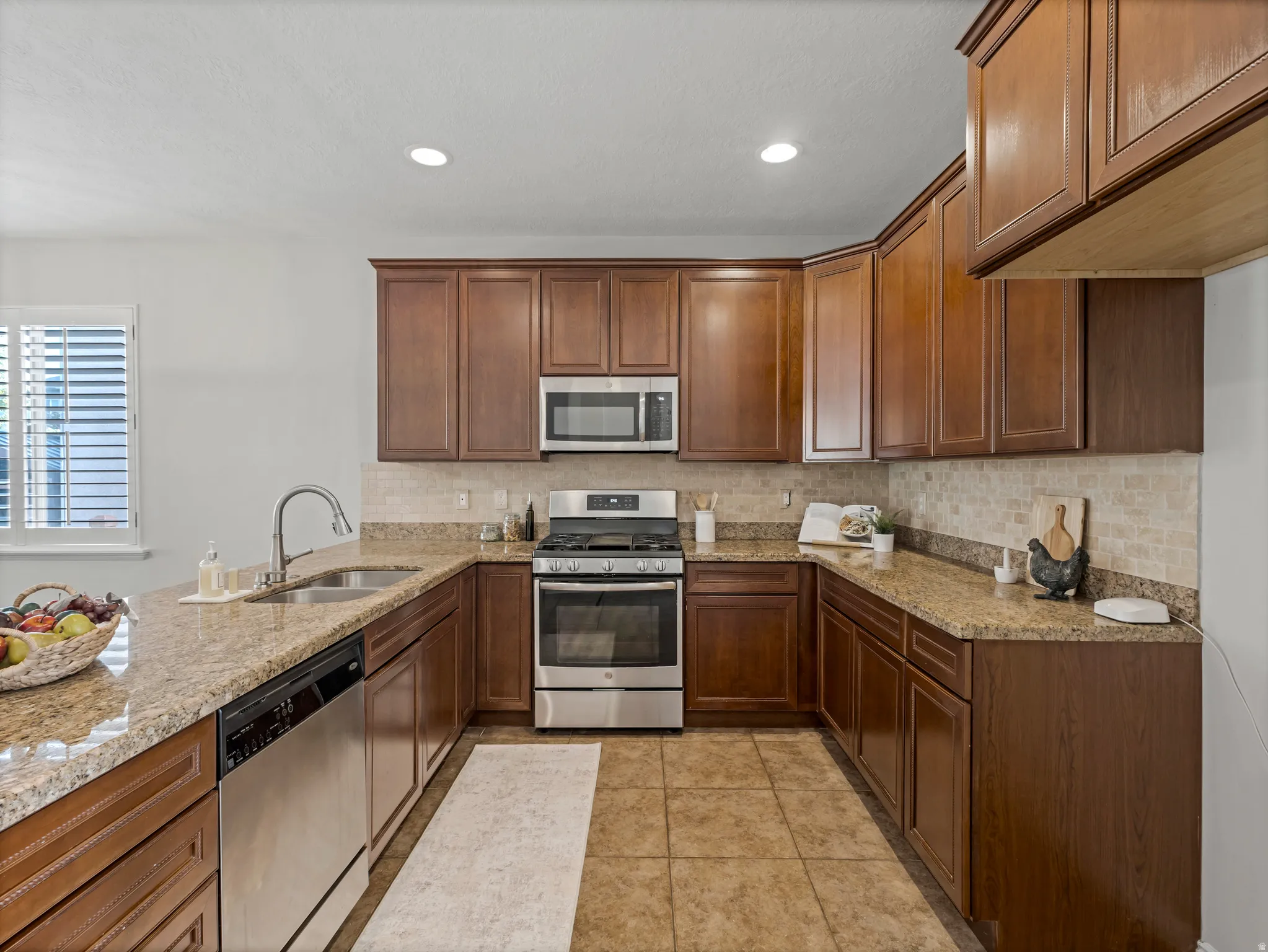 U-shaped kitchen featuring wood-finish cabinetry, granite countertops, tile backsplash, and stainless steel appliances including an oven range, microwave, and dishwasher