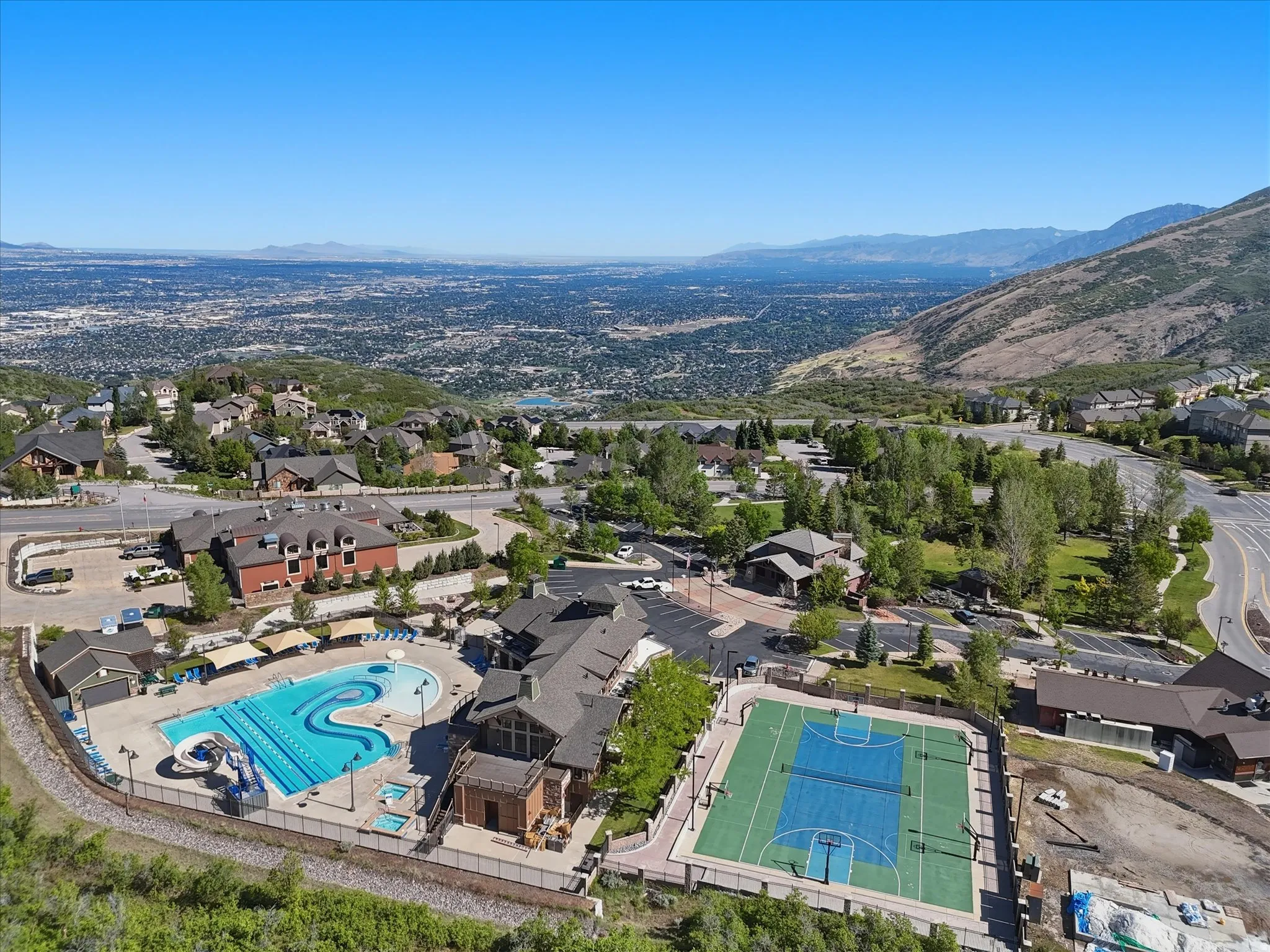 Community amenities featuring a resort-style swimming pool with multiple lanes and a winding slide, an adjacent multi-sport court, and surrounding structures with pitched roofs