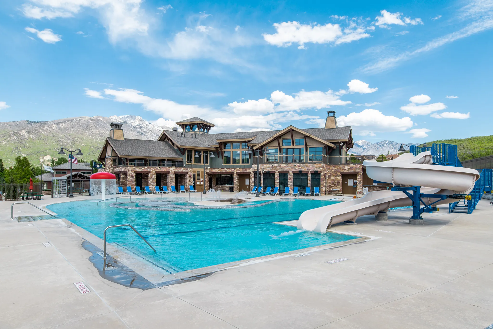 Outdoor swimming pool area featuring a large main pool, a children's splash feature, and two waterslides