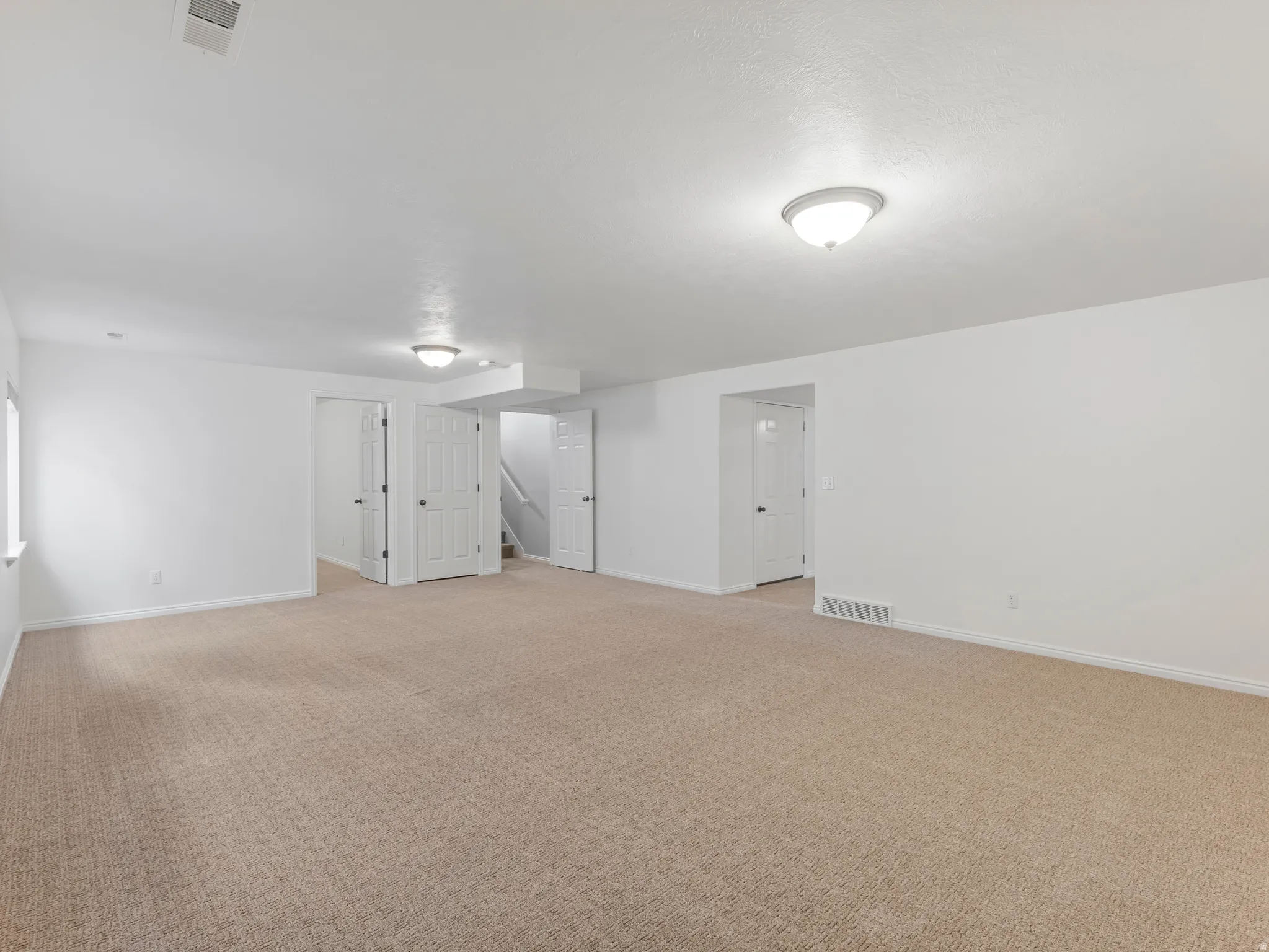 Expansive room featuring light-colored carpeting, white walls, and multiple entryways