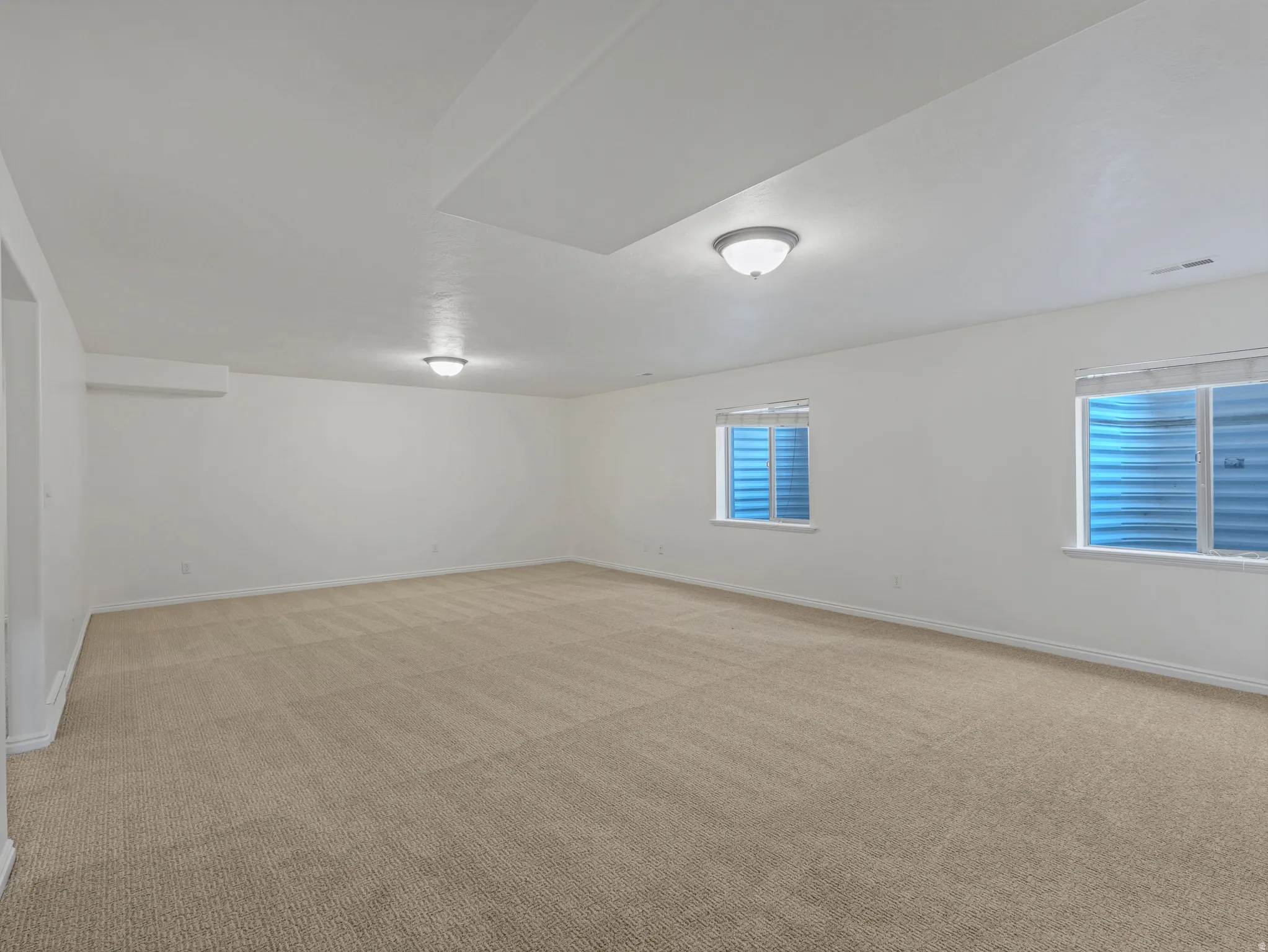 Spacious carpeted room featuring two egress windows, white walls, and flush-mount ceiling lighting