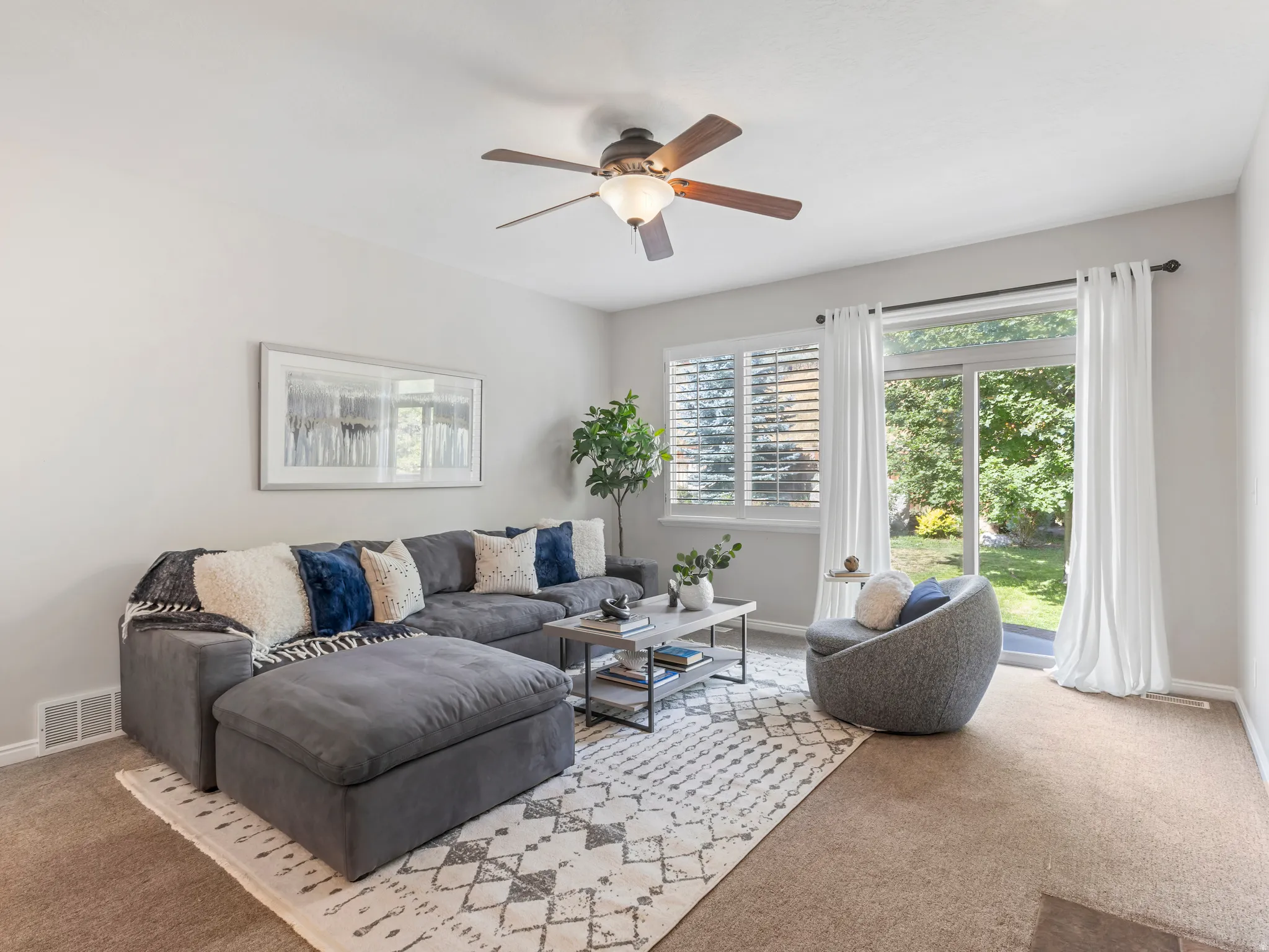 Carpeted living space featuring a ceiling fan with integrated lighting, a sliding glass door providing exterior access, and a window with white shutters