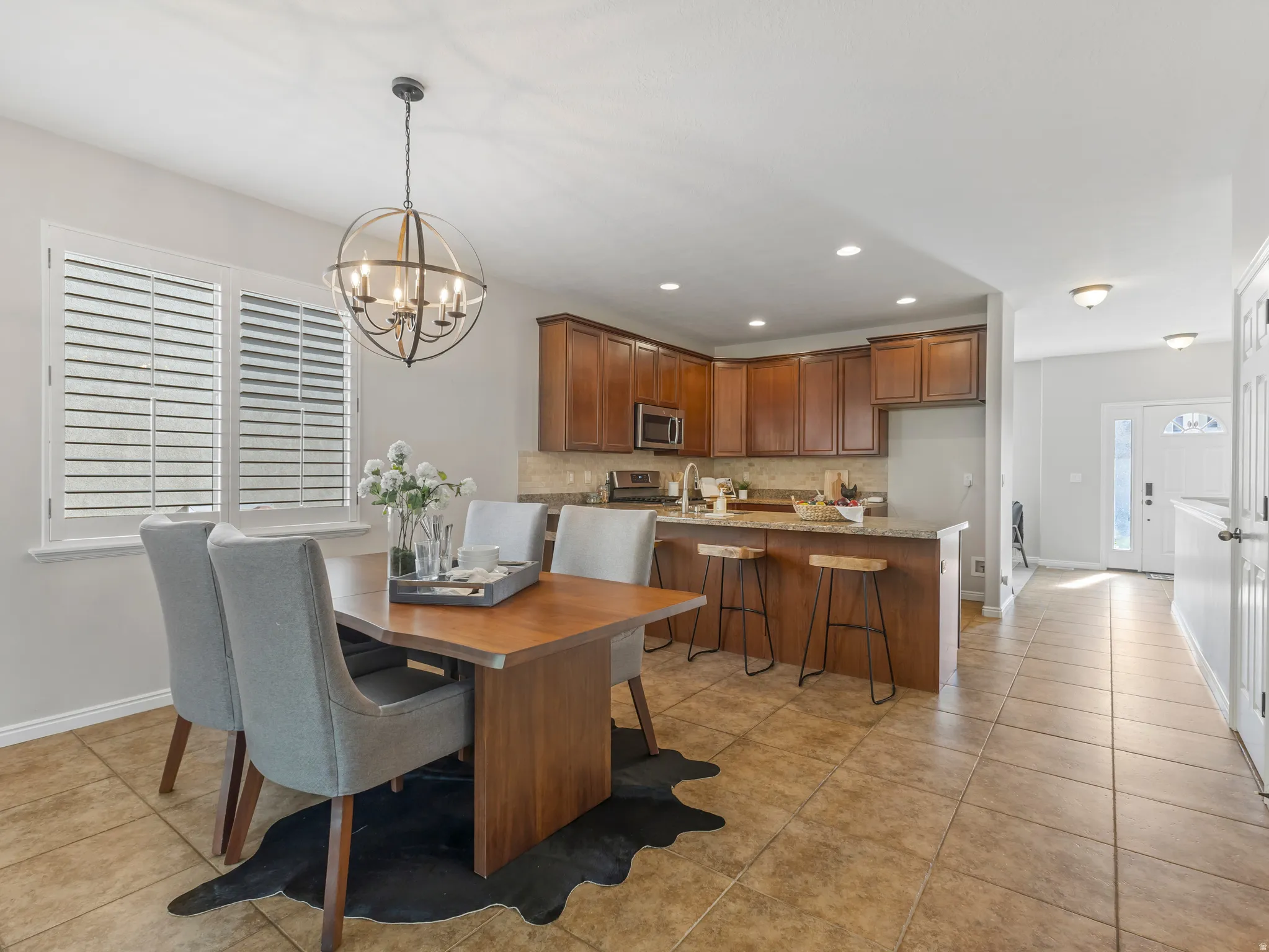 Open-concept kitchen and dining area featuring warm wood cabinetry, a breakfast bar with seating, a tile backsplash, and coordinating tile flooring