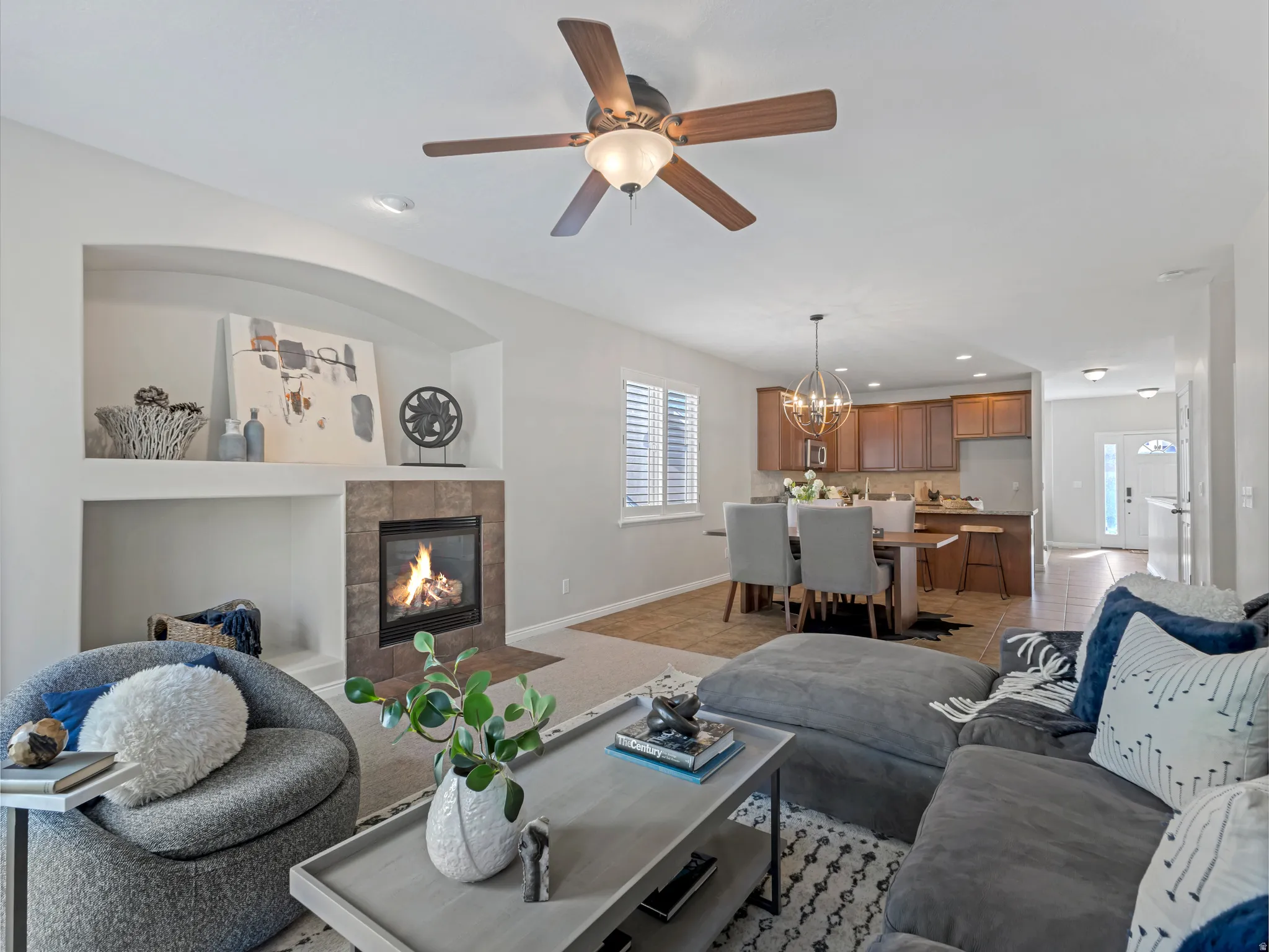 Living area featuring a tiled fireplace with an arched display niche above, a ceiling fan with integrated lighting, and carpet flooring