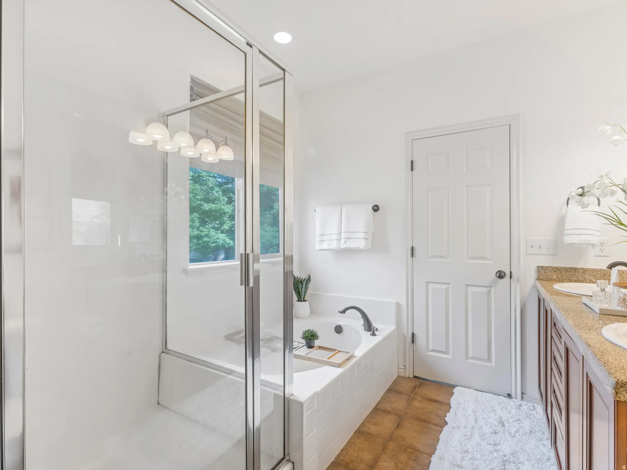 Bathroom featuring a glass-enclosed shower, built-in soaking tub, dual vanity with undermount sinks, stone-finish countertop, and tile flooring