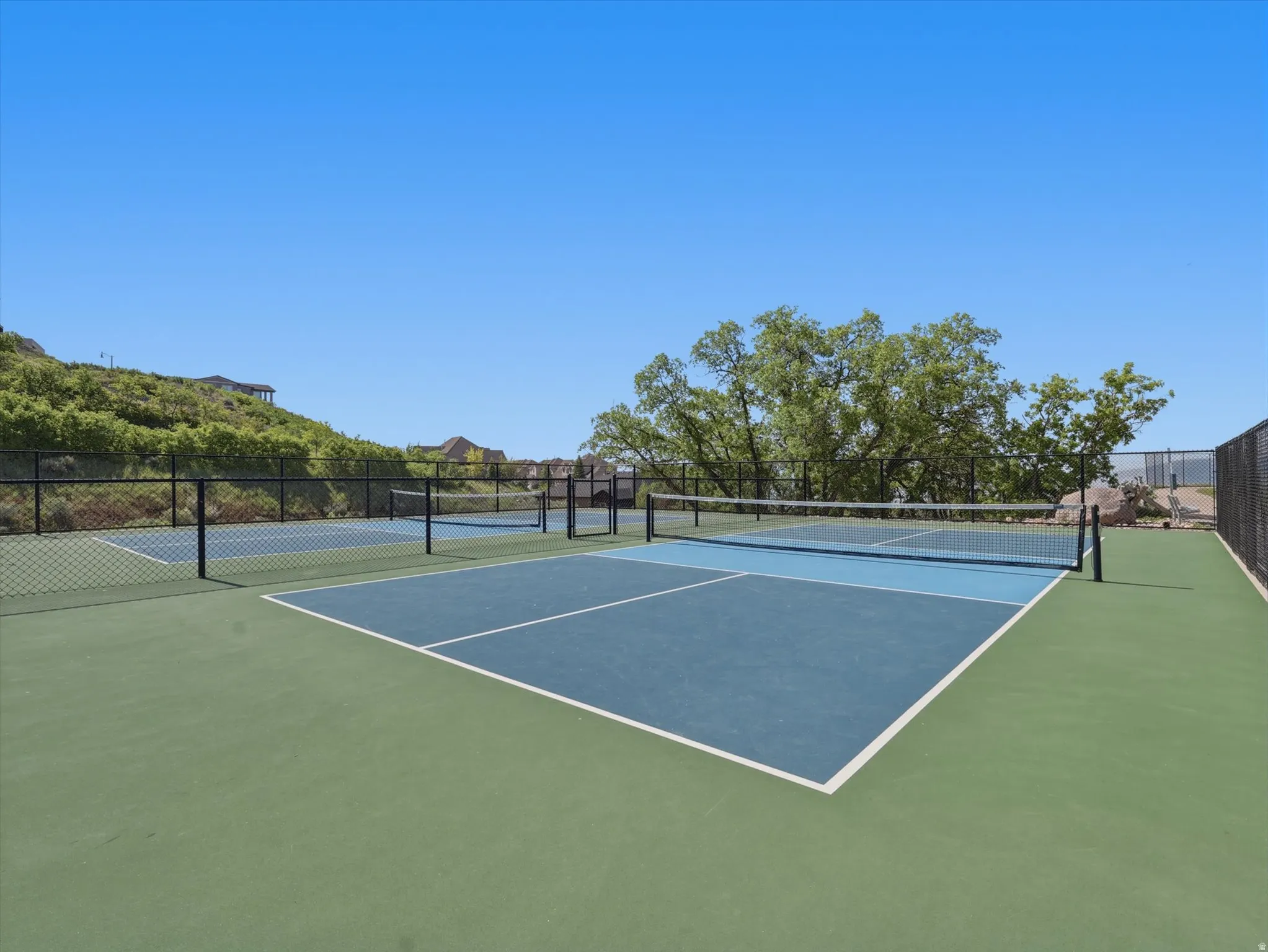 Multi-sport court featuring green and blue surfacing, white court lines, and a black net with posts