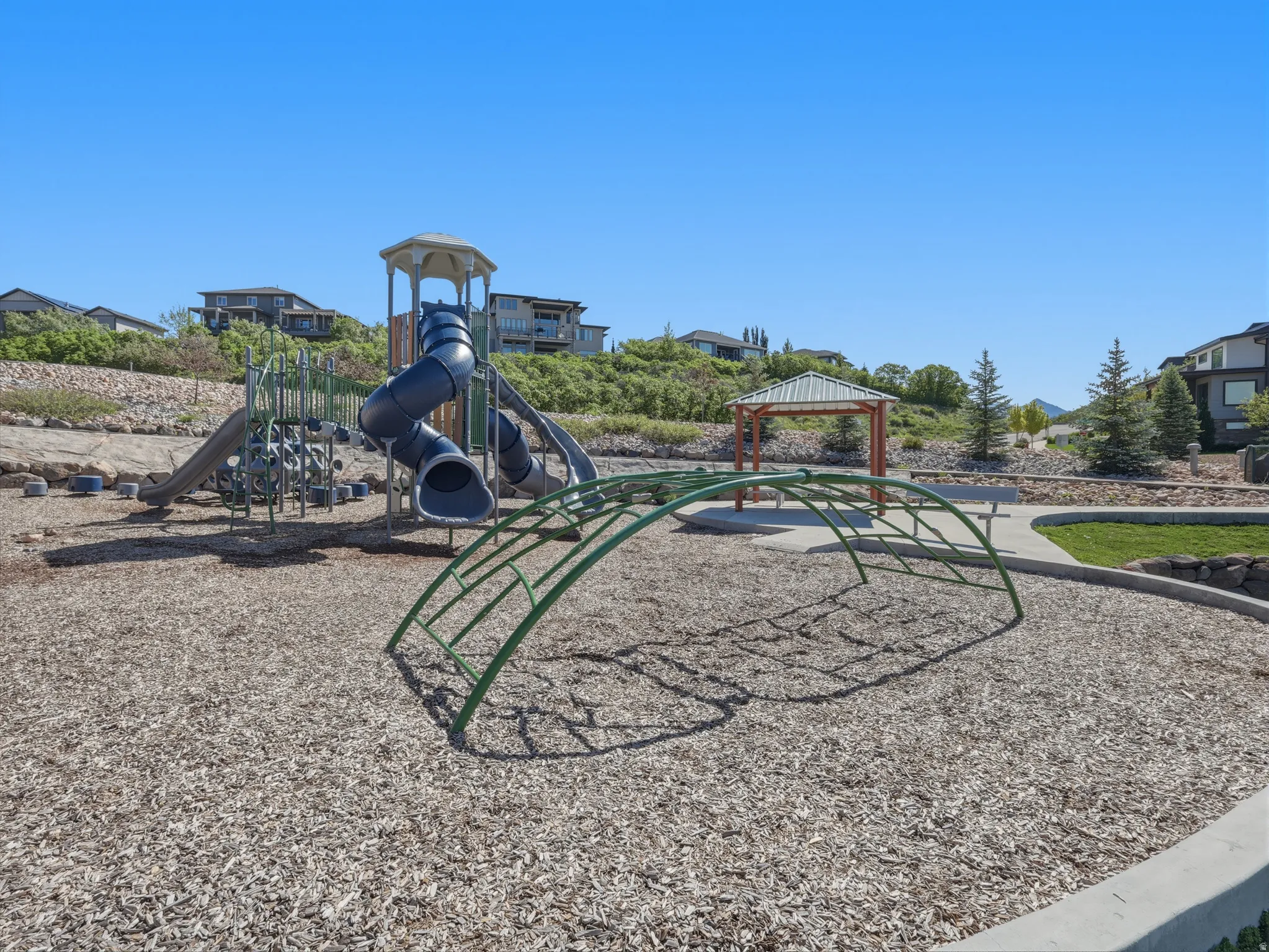Community playground featuring a multi-level play structure with slide, a separate climbing apparatus, and a shaded gazebo
