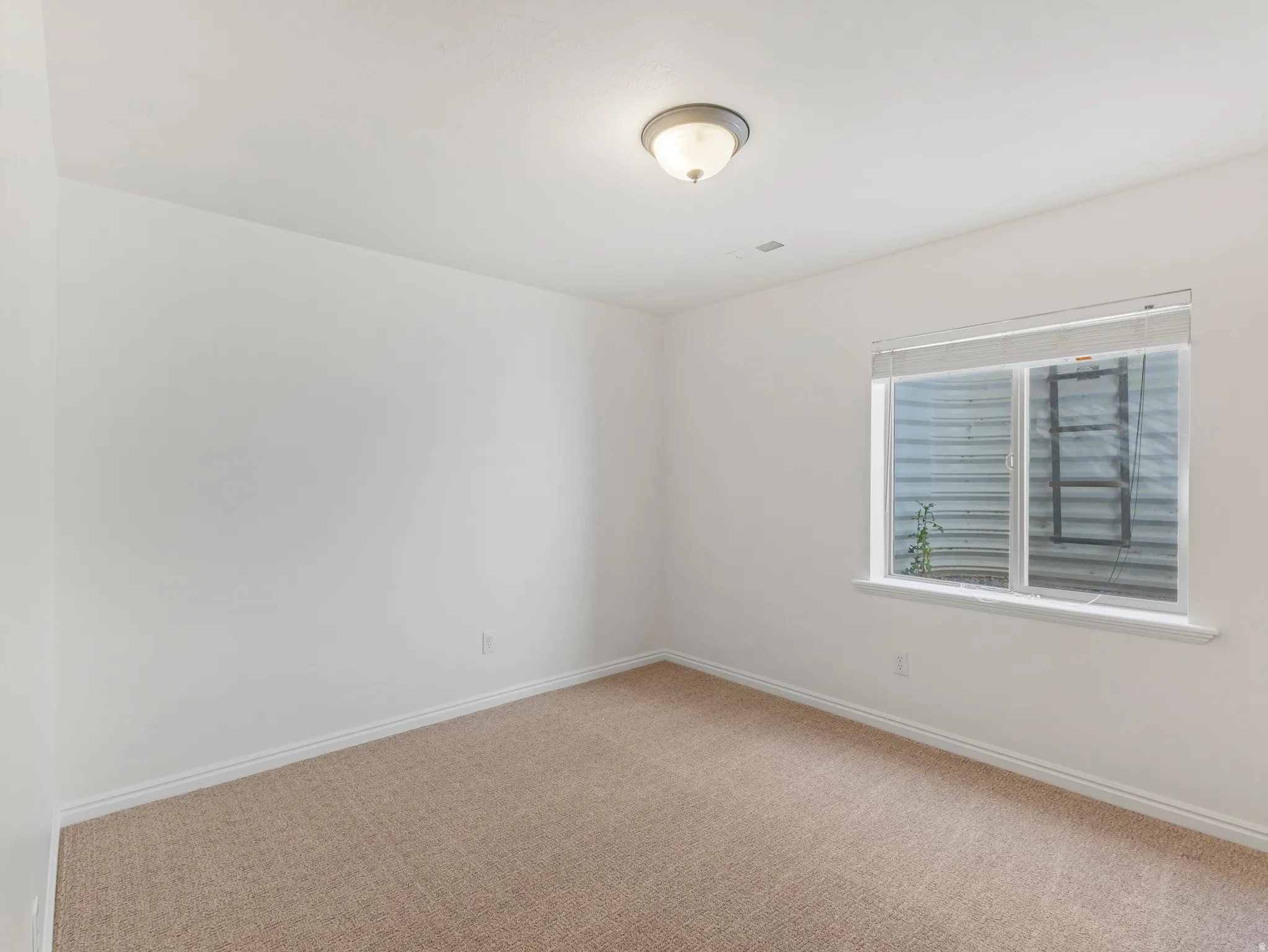 Carpeted room featuring a white ceiling and walls, a flush-mount ceiling light fixture, and a window with blinds