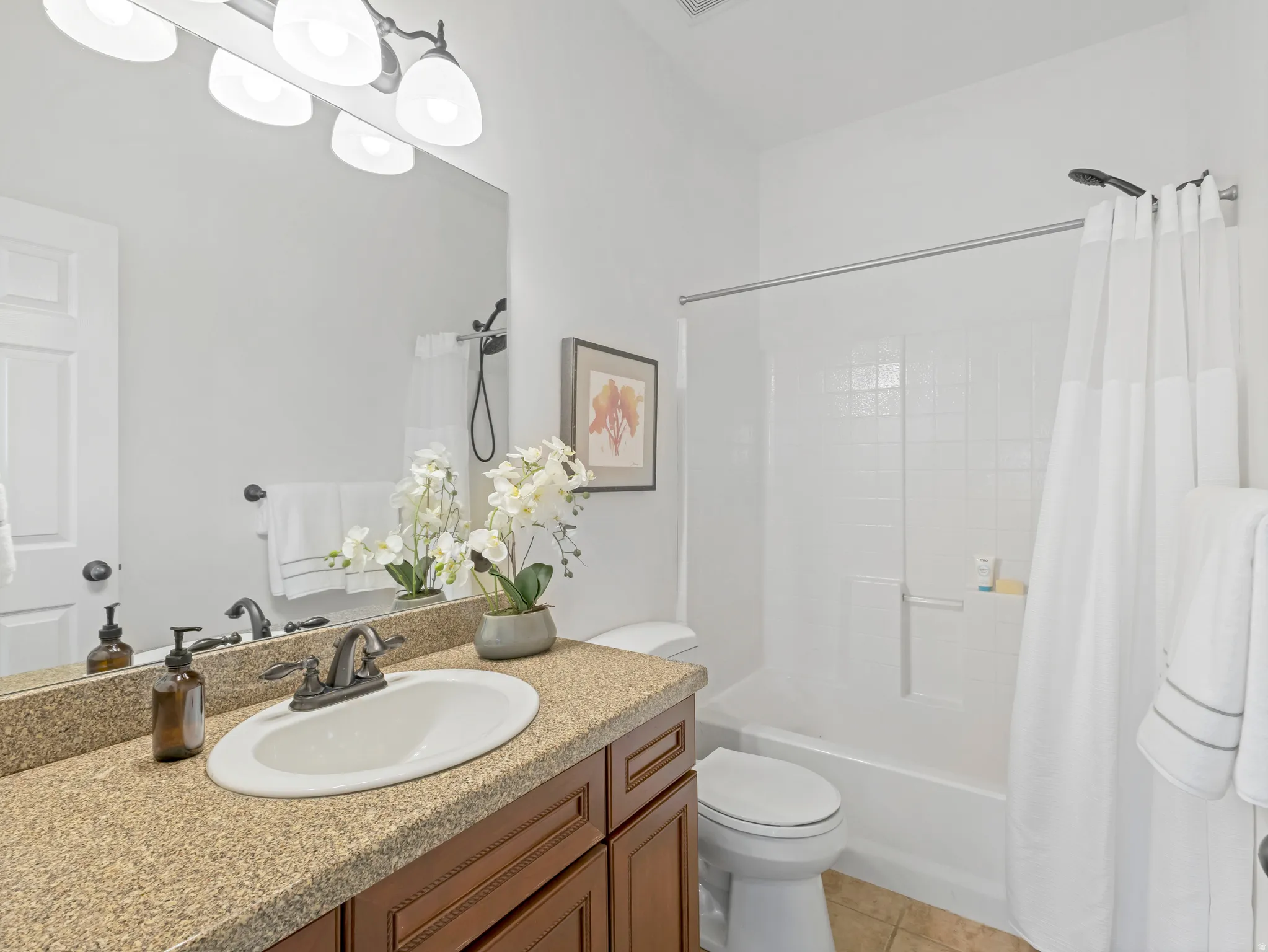 Bathroom featuring an oval undermount sink set in a speckled countertop, dark wood-finish cabinetry, and a full-size bathtub with white subway tile surround