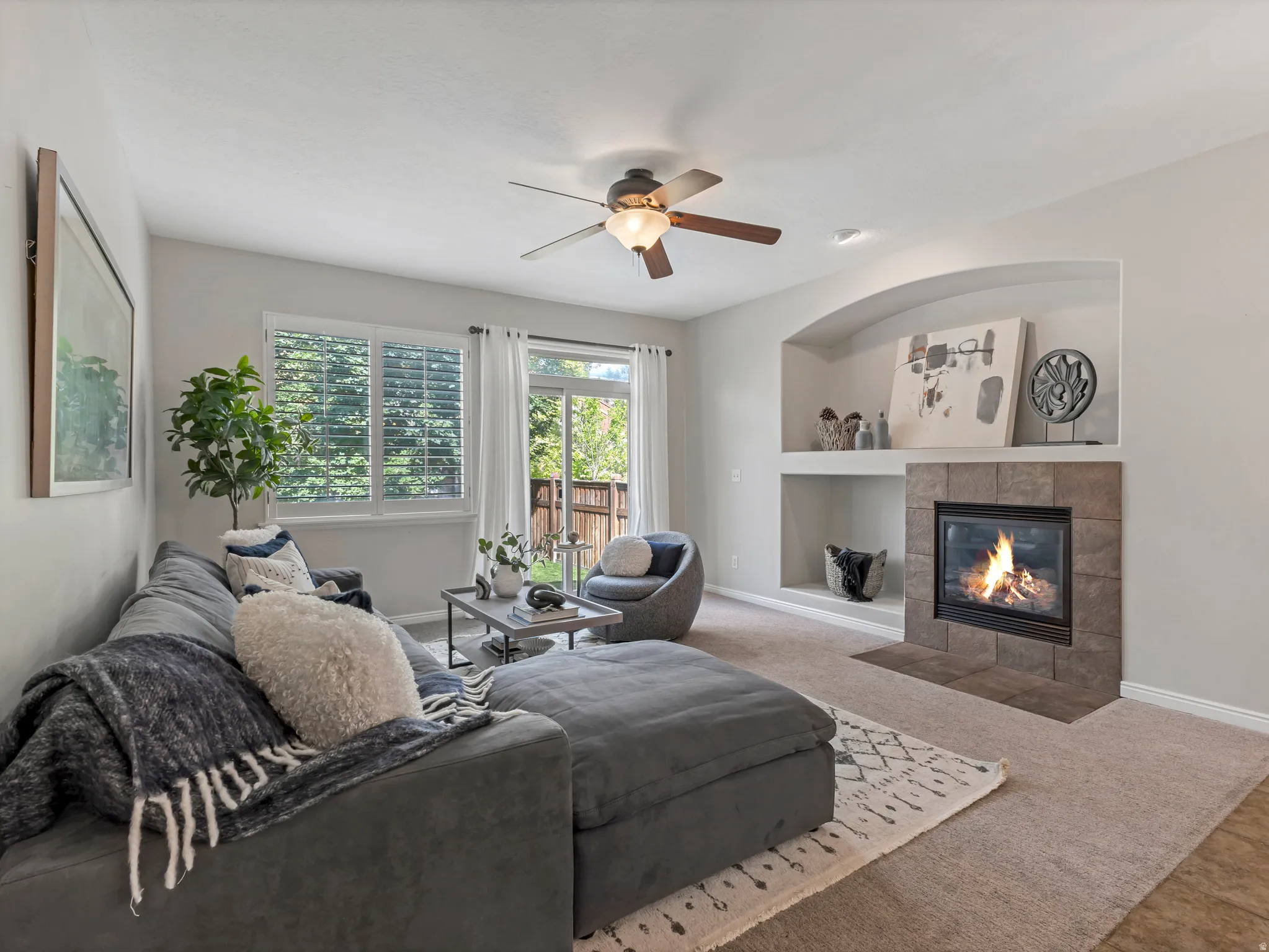 Living area featuring a stone-clad fireplace with hearth, arched built-in shelving, carpet flooring, and a ceiling fan