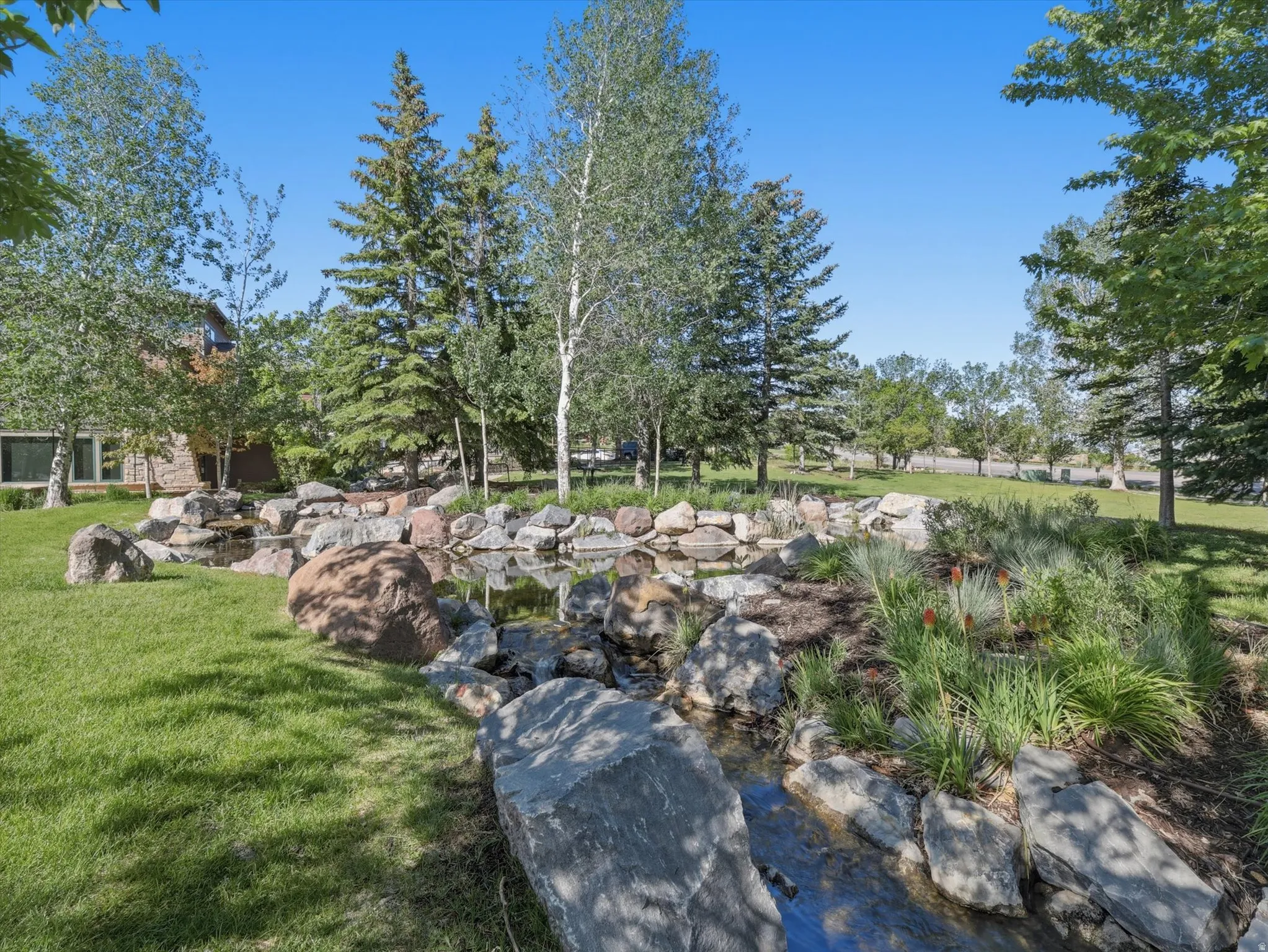 Naturalistic rock garden with a prominent water feature, surrounded by mature trees and lush green lawn