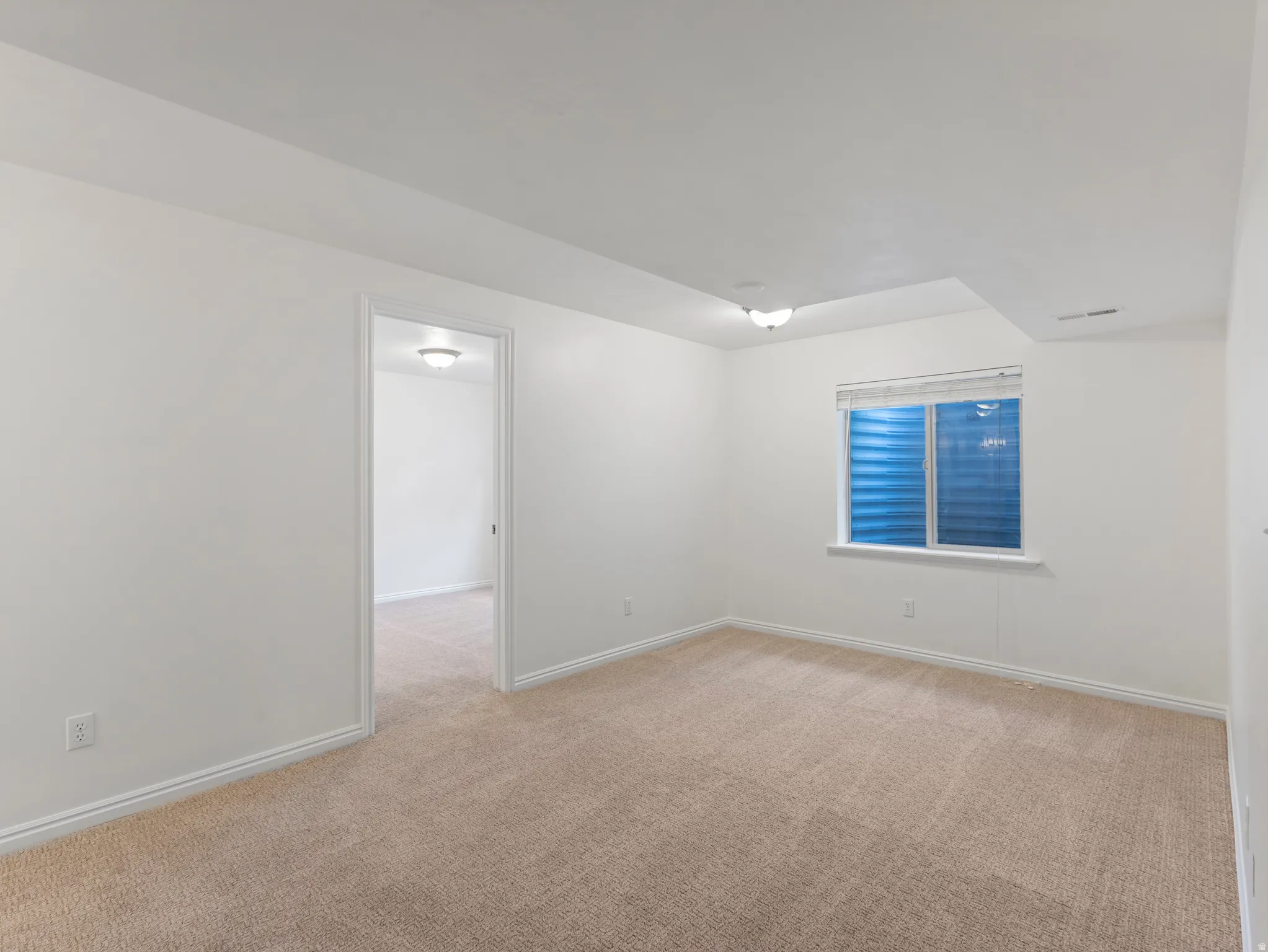 Carpeted room featuring a white window frame, white walls, and a ceiling-mounted light fixture