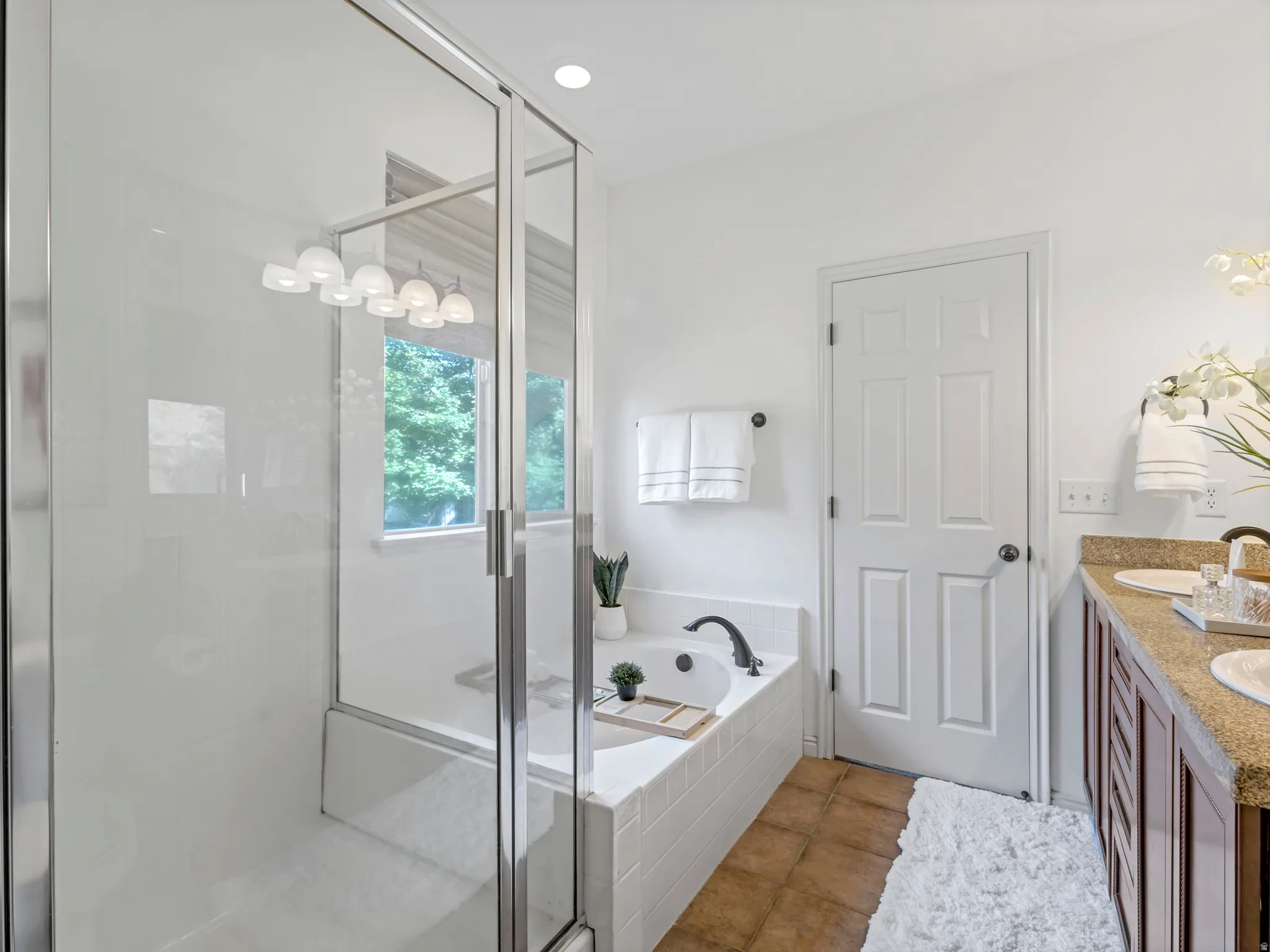 Modern bathroom featuring a glass-enclosed shower, a built-in soaking tub, a double vanity with granite-style countertops, wood cabinetry, and tile flooring