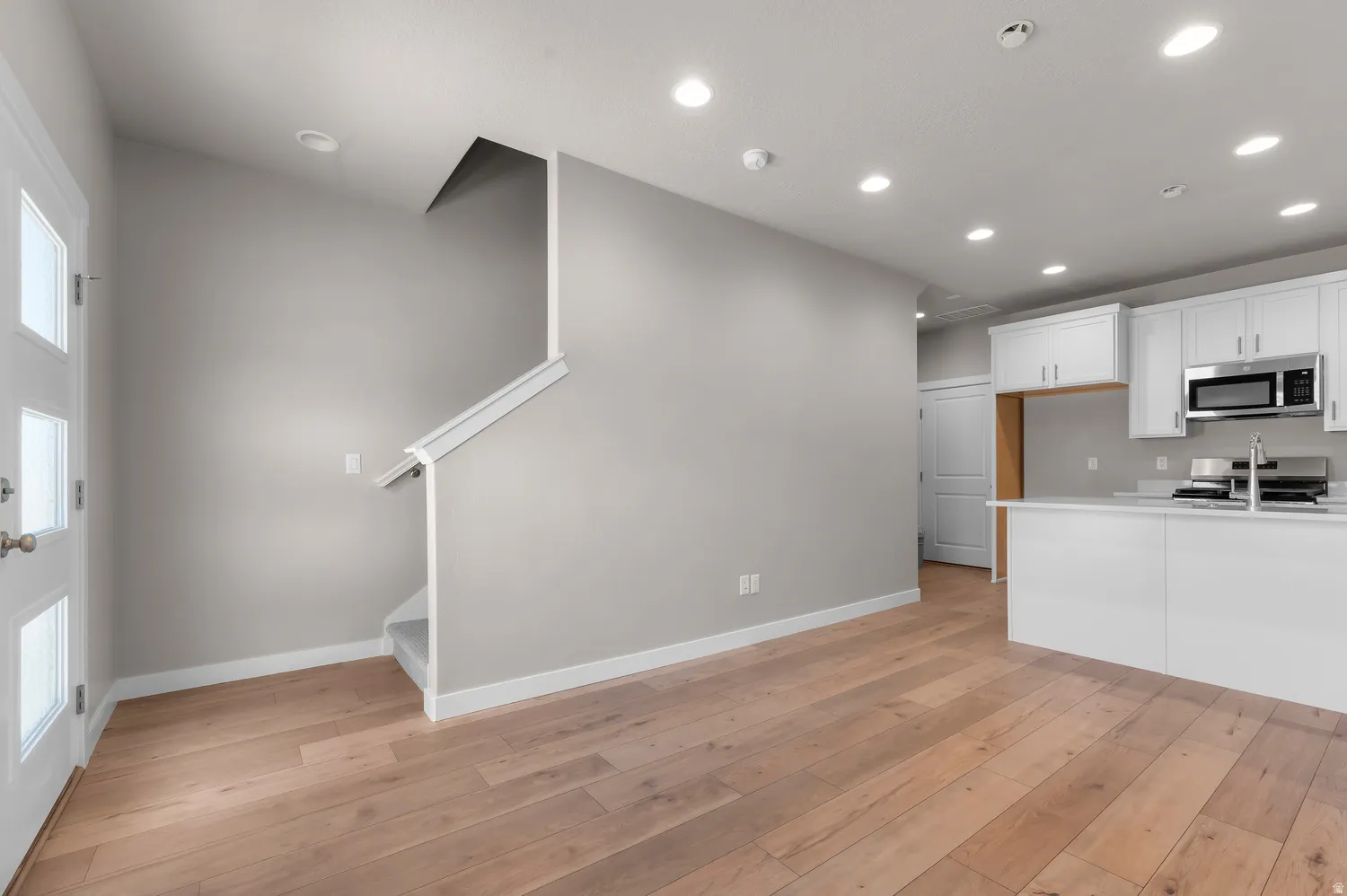 Wood-finish flooring throughout, recessed lighting, and a modern kitchen featuring white cabinetry, stainless steel appliances, and a kitchen island