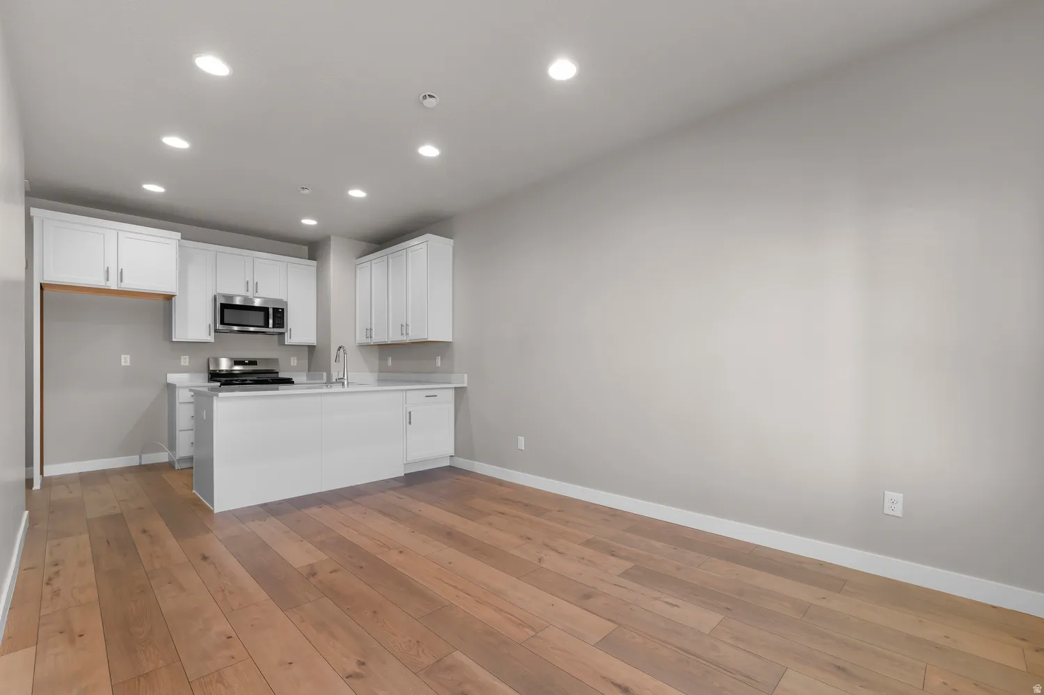 Kitchen with white cabinetry, stainless steel microwave, gas range, and a central island with a sink