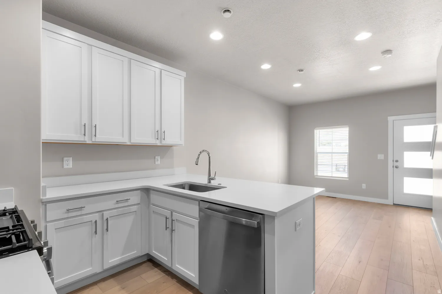 Open-concept kitchen featuring white cabinetry, light-toned countertops, and stainless steel appliances
