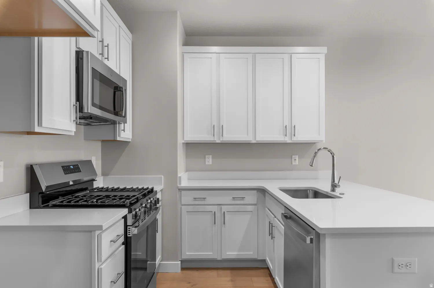 White shaker-style cabinetry with chrome hardware, stainless steel appliances, and light-toned countertops