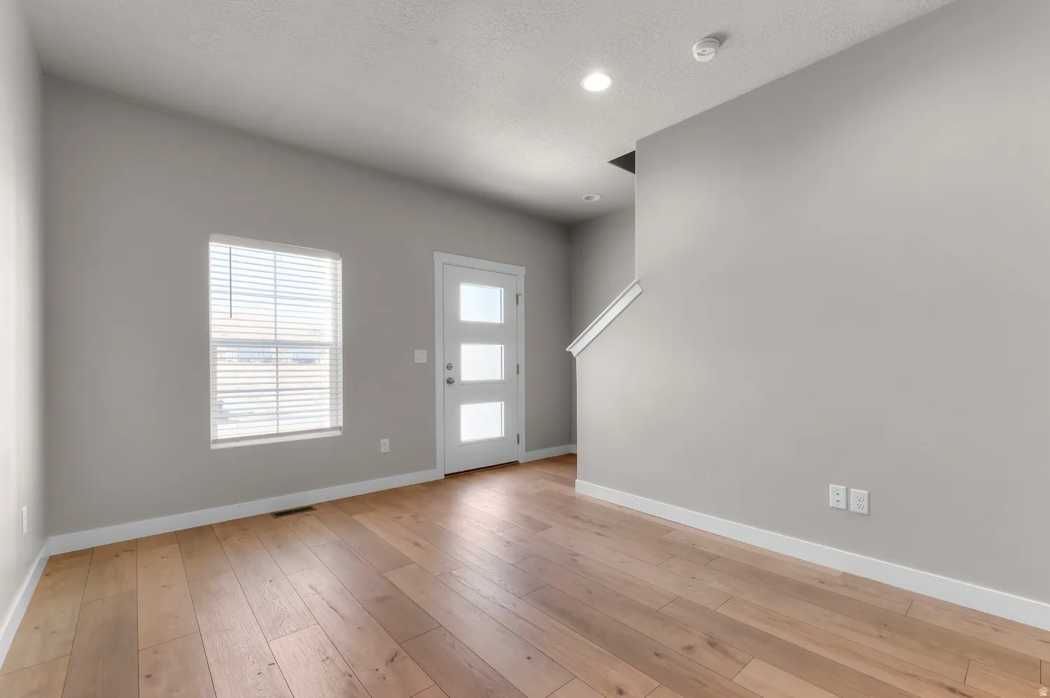 Wood-finish flooring, contemporary light gray wall paint, white trim, recessed lighting, and a modern entry door with frosted glass panels