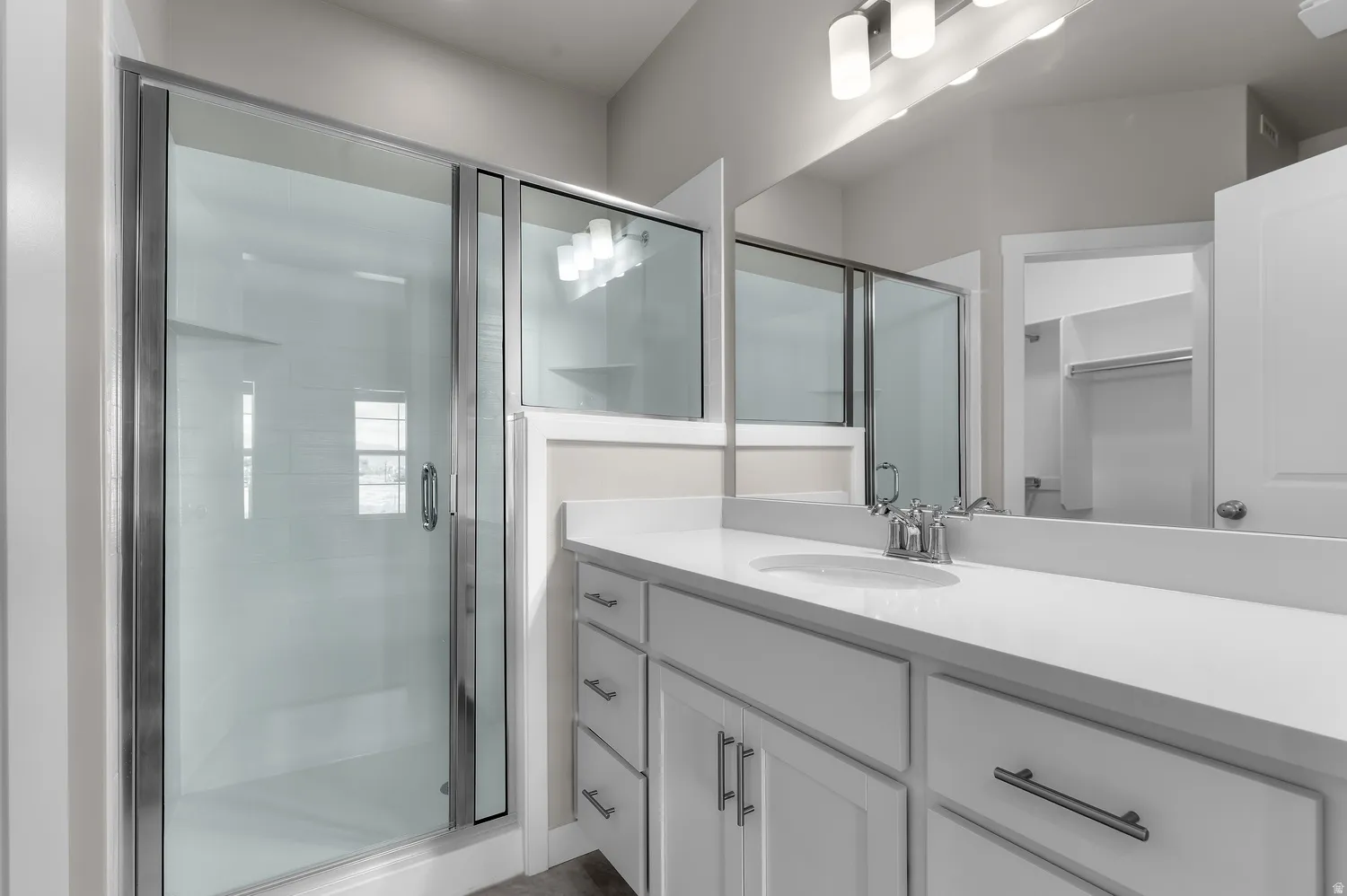 Walk-in shower with sliding glass door, vanity with dual sinks, expansive counter space, white cabinetry, and a large mirror