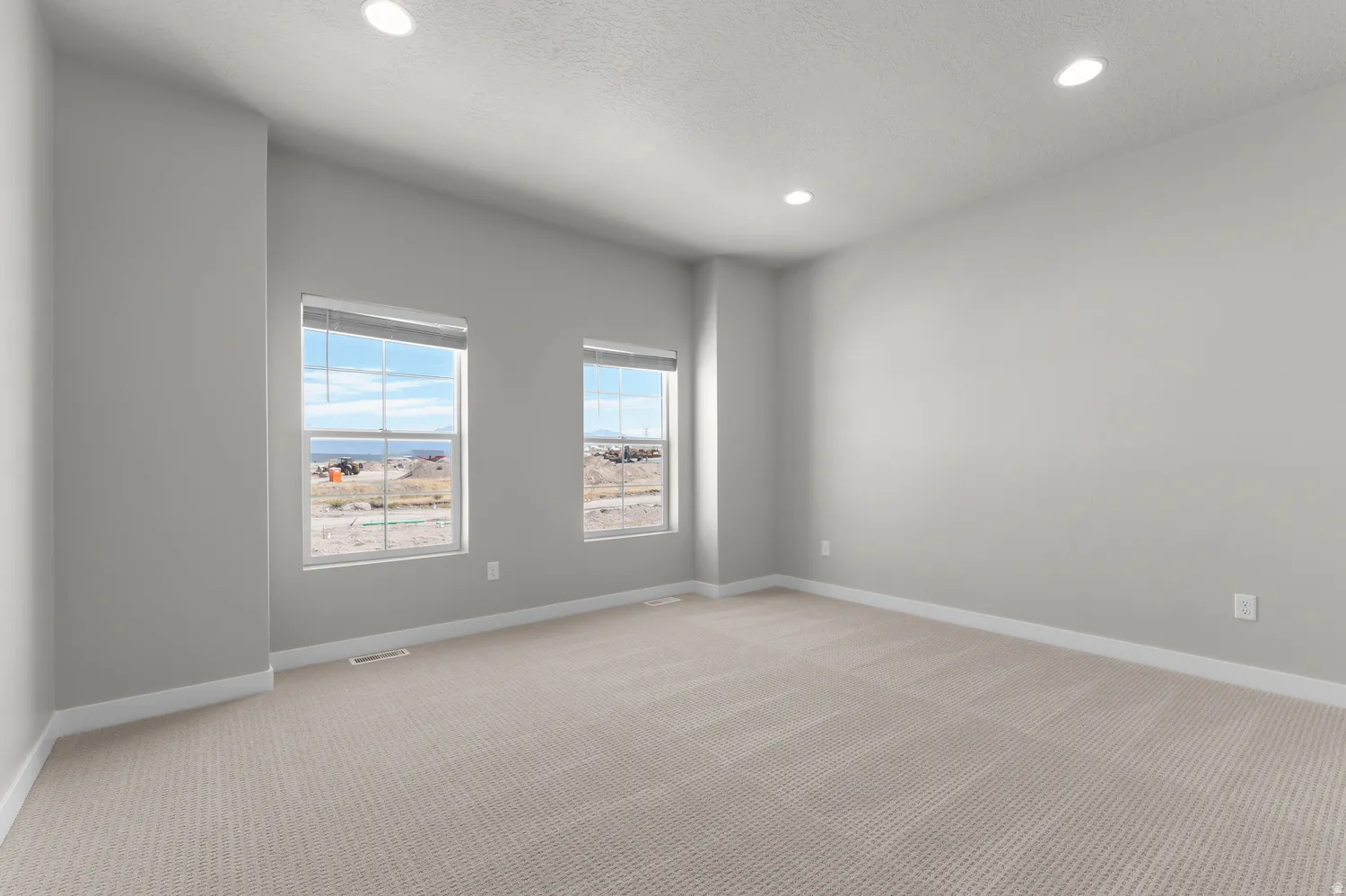 Recessed lighting illuminating neutral wall tones, two windows with blinds, and light-toned carpet flooring