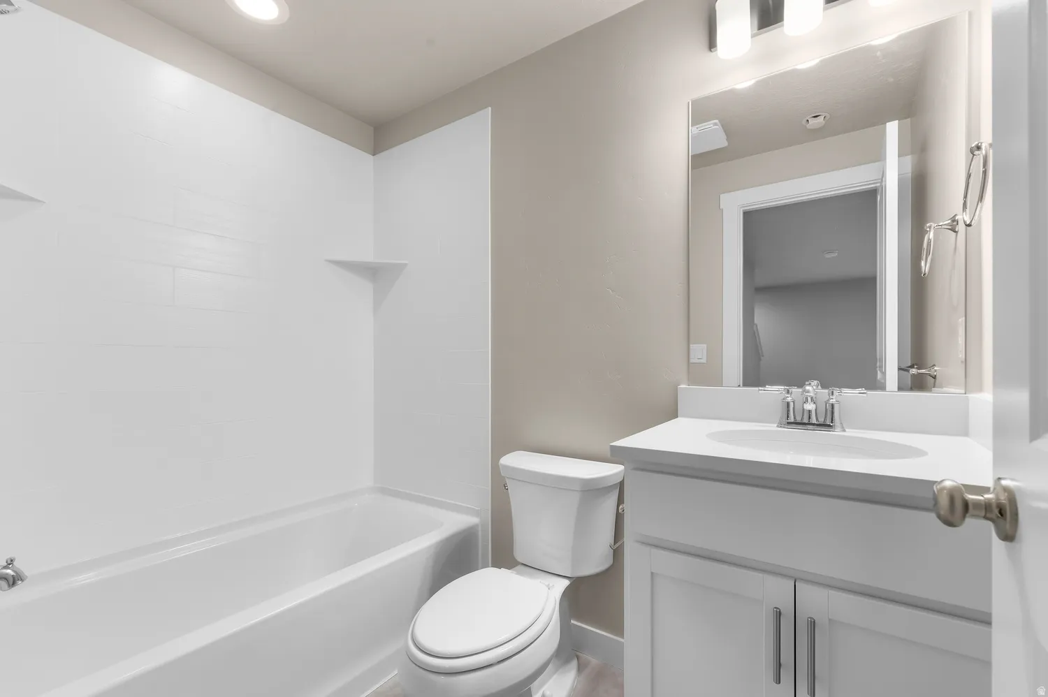 White tile shower surround, integrated bathtub, white vanity with an undermount sink, wall-mounted mirror, and a modern light fixture