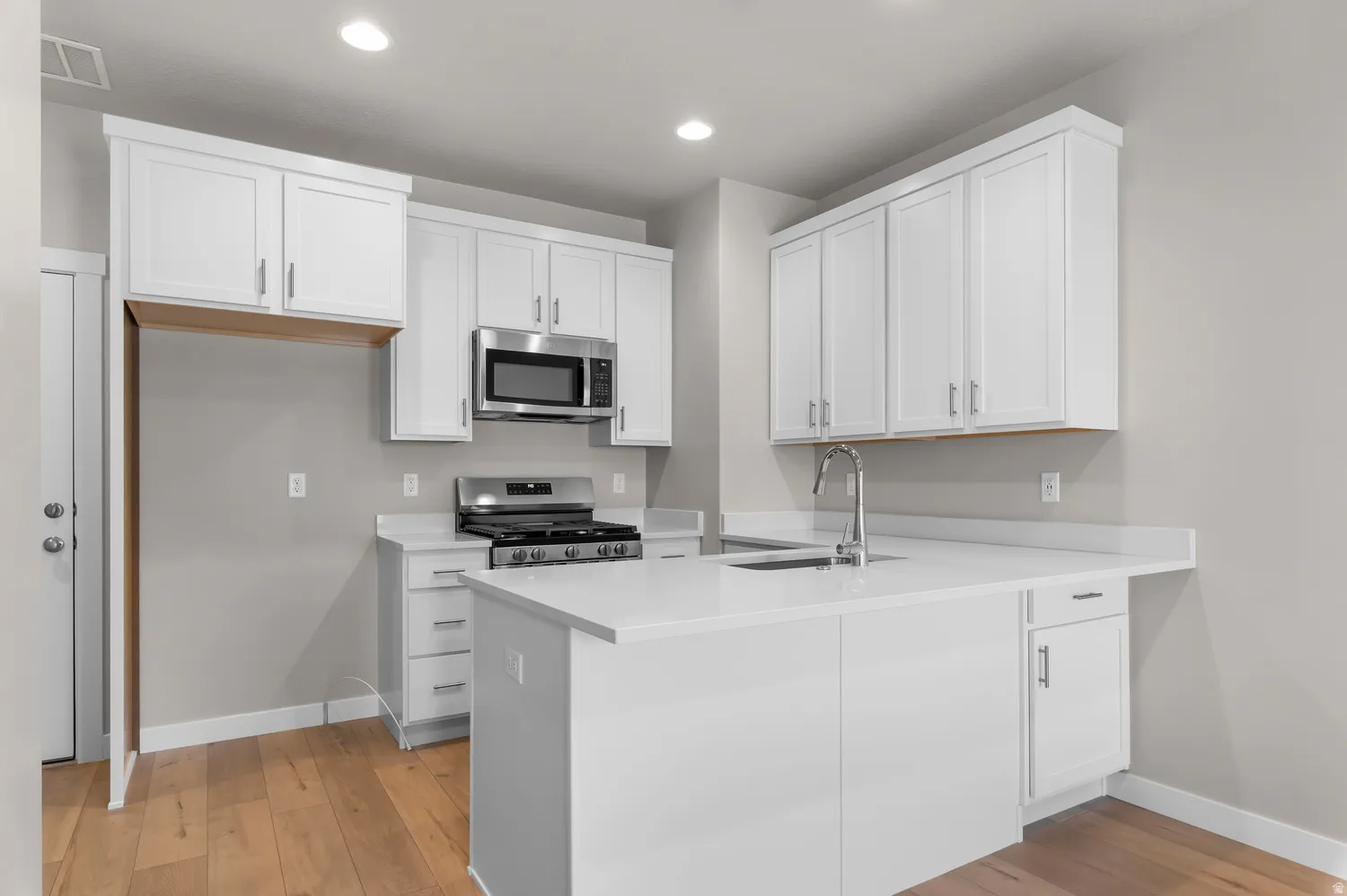 Kitchen featuring white cabinetry, stainless steel appliances, a center island with sink, light-toned countertops, and wood-finish flooring