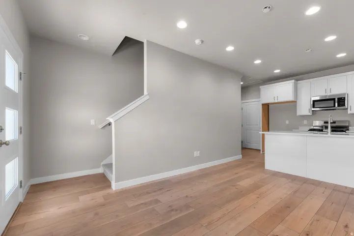 Wood-finish flooring throughout, recessed lighting, and a modern kitchen featuring white cabinetry, stainless steel appliances, and a kitchen island