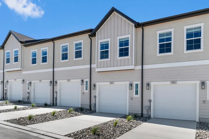 Contemporary townhome exterior featuring light-colored siding, stucco accents, white-framed windows, individual garage doors, and exterior lighting fixtures