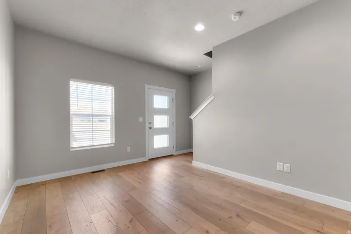 Wood-finish flooring, contemporary light gray wall paint, white trim, recessed lighting, and a modern entry door with frosted glass panels