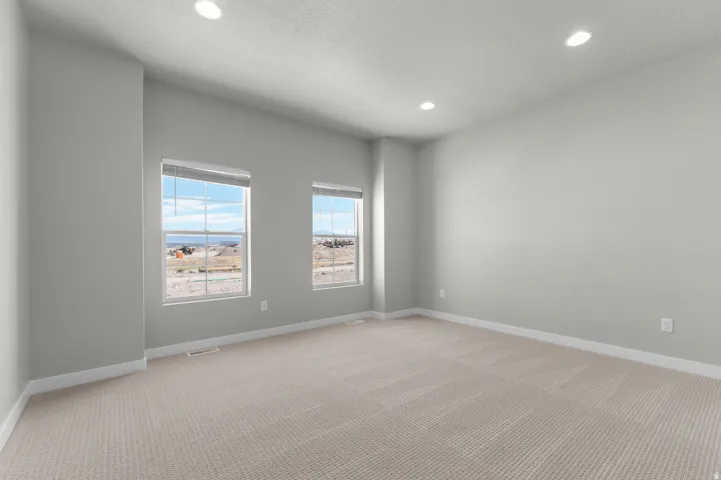 Recessed lighting illuminating neutral wall tones, two windows with blinds, and light-toned carpet flooring