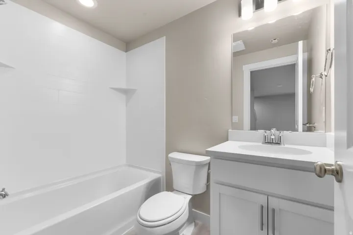 White tile shower surround, integrated bathtub, white vanity with an undermount sink, wall-mounted mirror, and a modern light fixture