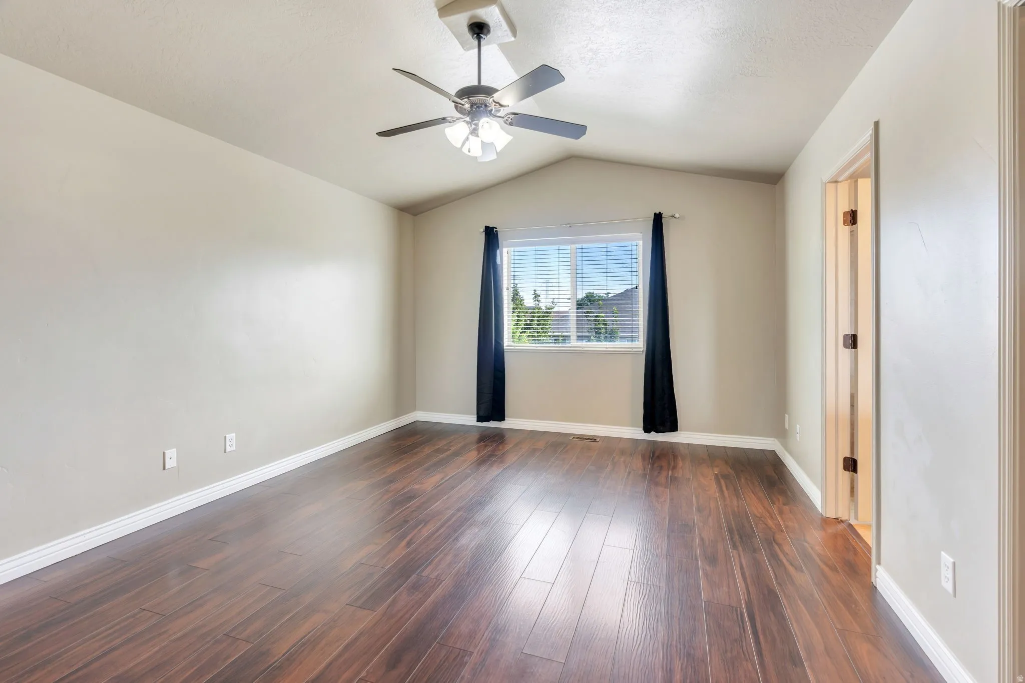 Spacious room featuring wood-finish flooring, a vaulted ceiling, and a ceiling fan with integrated lighting