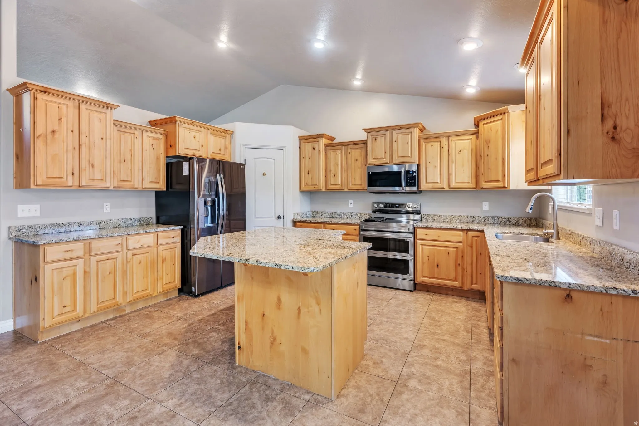Spacious kitchen featuring an island, light wood cabinetry, stone countertops, stainless steel appliances, and tile flooring