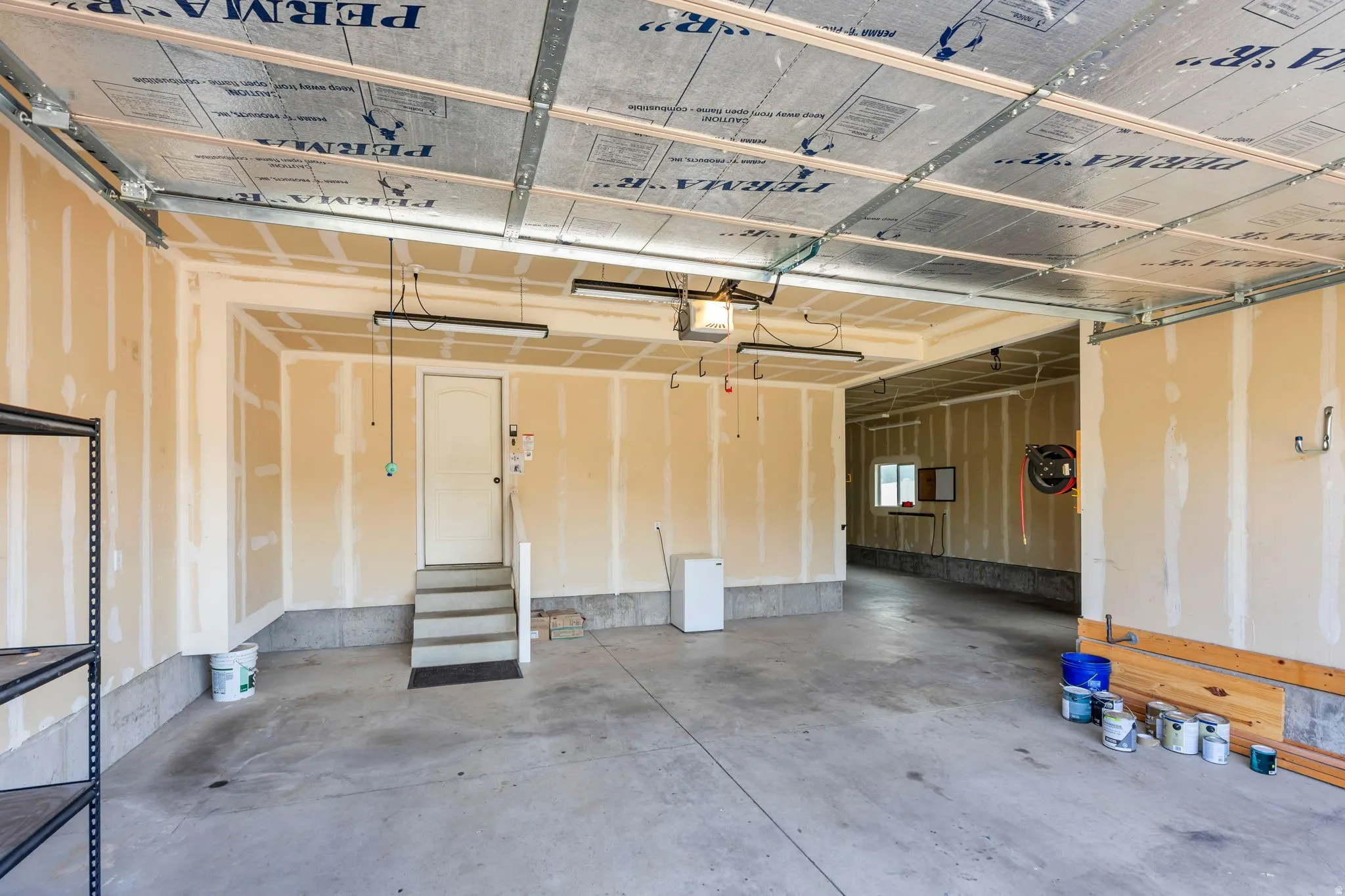 Spacious garage featuring a concrete floor, exposed joist ceiling with insulation, and unfinished drywall walls