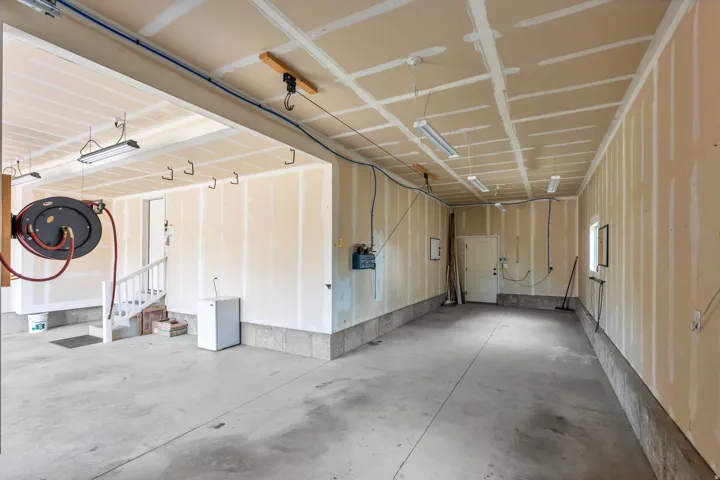 Expansive concrete floor garage space with fluorescent lighting, partial drywall, and multiple utility access points