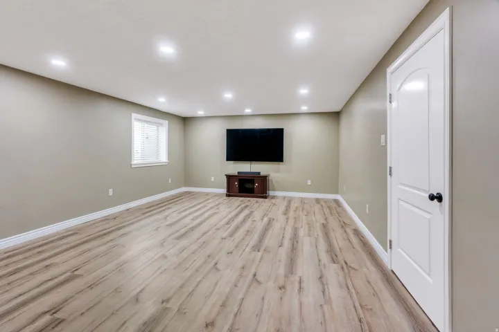 Spacious room featuring wood-finish flooring, recessed lighting, and a white interior door with a black knob