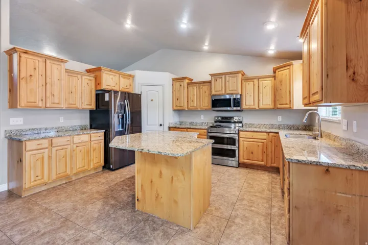 Spacious kitchen featuring an island, light wood cabinetry, stone countertops, stainless steel appliances, and tile flooring