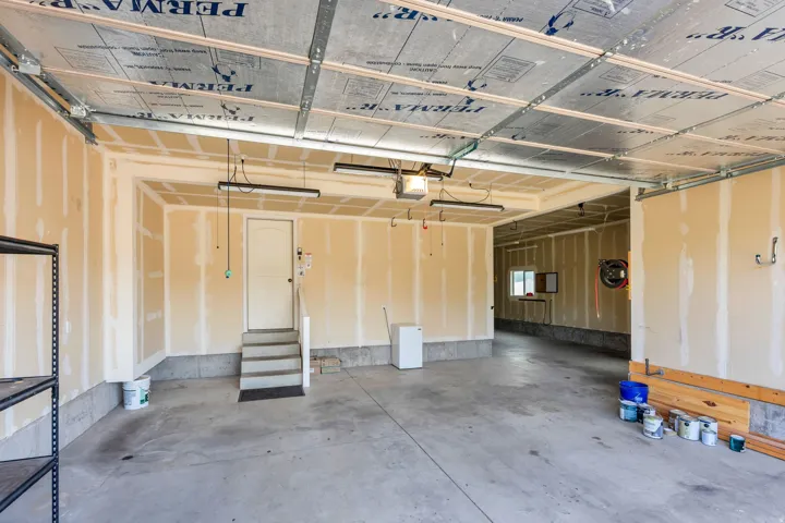 Spacious garage featuring a concrete floor, exposed joist ceiling with insulation, and unfinished drywall walls