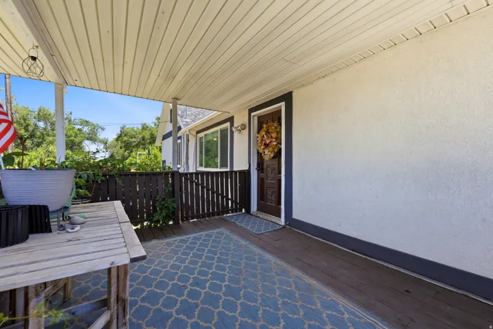 Covered front porch featuring a decorative wood entry door, stucco exterior, slatted wood railings, and a wood-finish floor